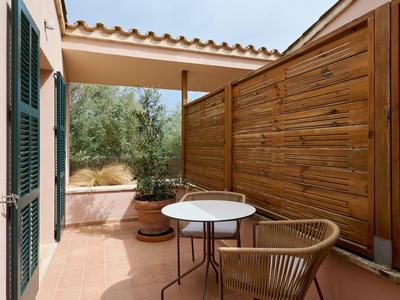 Útulná terasa s dřevěným plotem, malým kulatým stolem a proutěným křeslem.