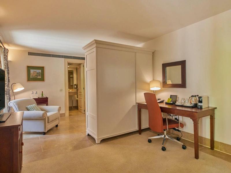 Hotelový pokoj s útulnou sedací částí, pracovním stolem se židlí a teplým osvětlením.