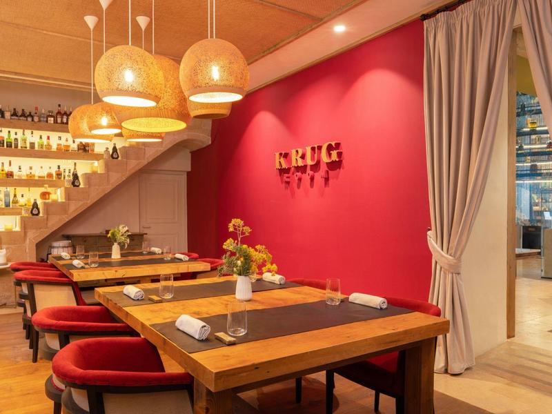 Příjemná hotelová restaurace s dřevěnými stoly, červenými zdmi a moderními závěsnými lampami pod schody.