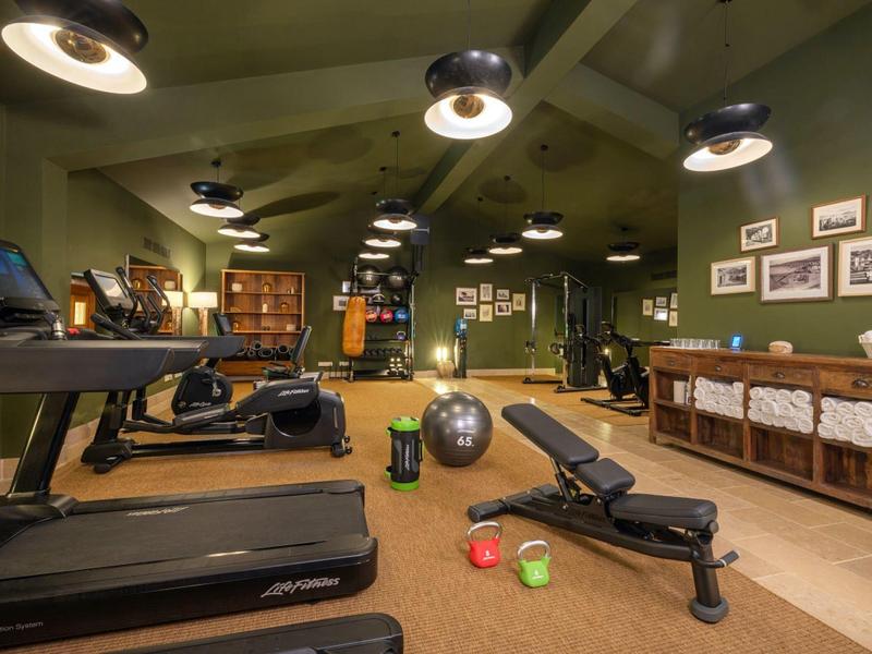 Dobře vybavená posilovna s běžeckými pásy, činkami, gymnastickými míči a ručníky na policích.