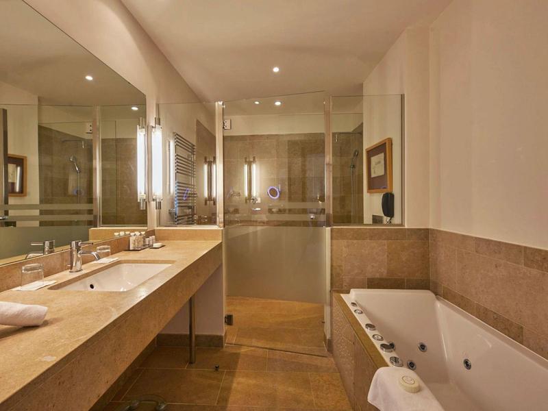 Moderní koupelna s dvojitým umyvadlem, velkým zrcadlem a vanou s ručníkem.