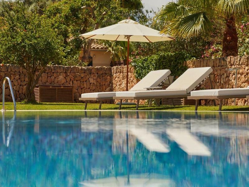 Bazén s lehátky a slunečníkem před kamennou zdí a zelení.