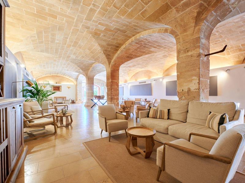 Elegantní hotelový salonek s béžovými pohovkami, křesly, kamennými oblouky a teplým osvětlením.