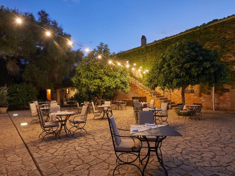 Pohodlná venkovní sezení s řetězem světel, stromy a kamennou podlahou za soumraku.