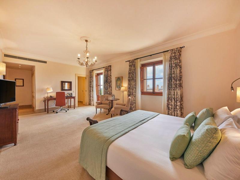 Prostorný hotelový pokoj s velkou postelí, posezením, pracovním stolem a elegantním zařízením.