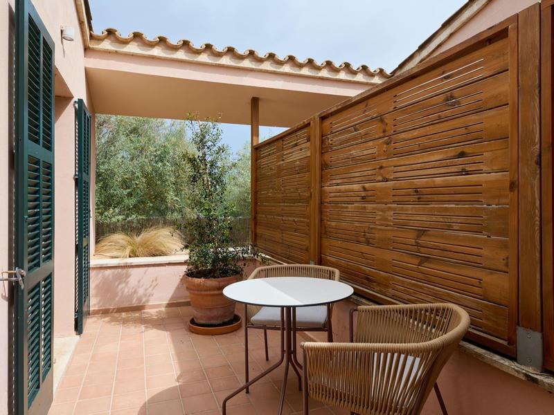 Útulná terasa s dřevěným plotem, malým kulatým stolem a proutěným křeslem.