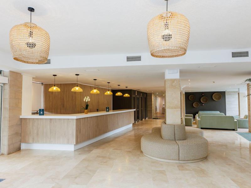 Recepción amplia y luminosa de hotel con suelo de mármol y lámparas colgantes decorativas.