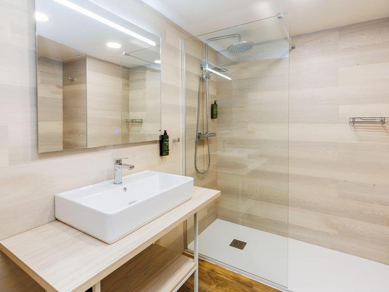 Baño moderno con lavabo rectangular y ducha accesible con mampara de vidrio.