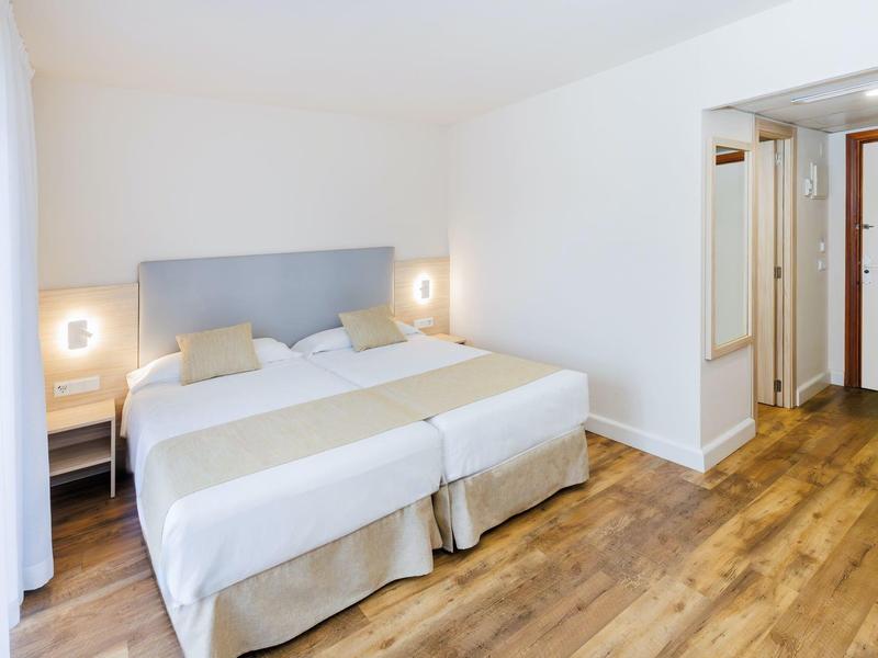 Habitación de hotel luminosa con dos camas individuales, suelo de madera y decoración minimalista.