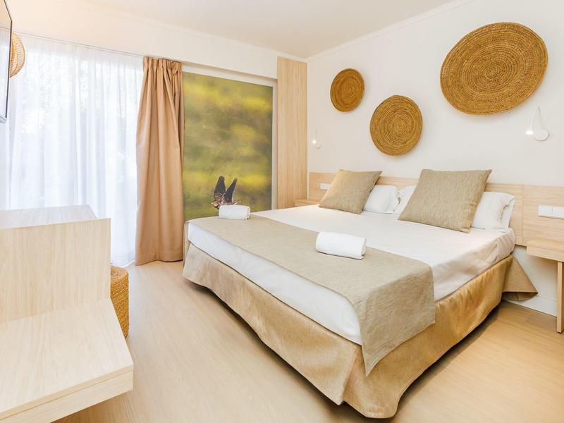 Habitación de hotel iluminada con cama grande, decoración de pared de materiales trenzados y ventana amplia.