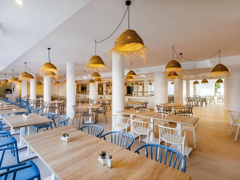 Restaurante de hotel moderno y luminoso con muebles de madera y metal y lámparas colgantes doradas.