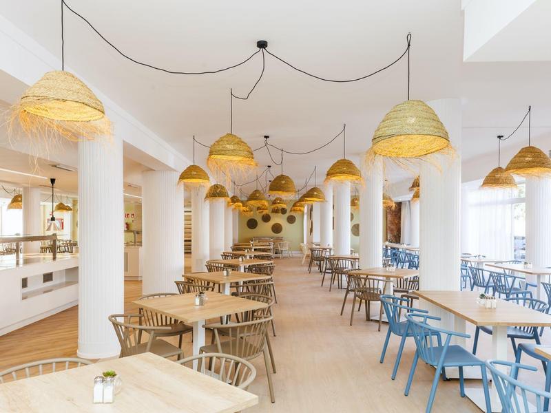 Comedor moderno y luminoso con sillas de madera, bancos azules y grandes lámparas de mimbre.