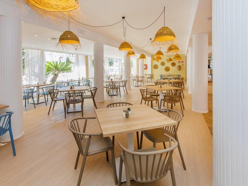 Amplio comedor de hotel con mesas de madera y sillas, decorado con lámparas colgantes amarillas.