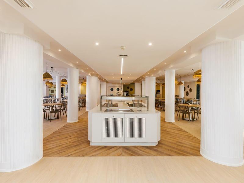 Interior moderno de un restaurante espacioso y luminoso con columnas blancas y suelo de madera.