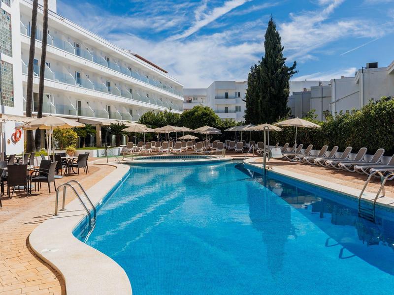 Gran piscina exterior con tumbonas y sombrillas junto a un edificio de hotel de varios pisos.
