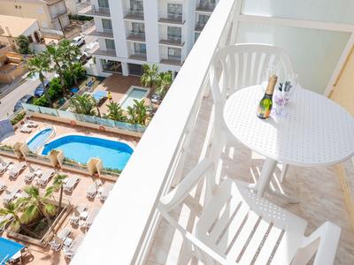 Balkon mit weißem Tisch und Stühlen blickt auf Pool und Sonnenliegen in einem Hotel.