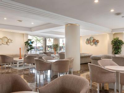 Área de descanso moderna y luminosa del hotel con sillones suaves, mesas y elementos decorativos en la pared.