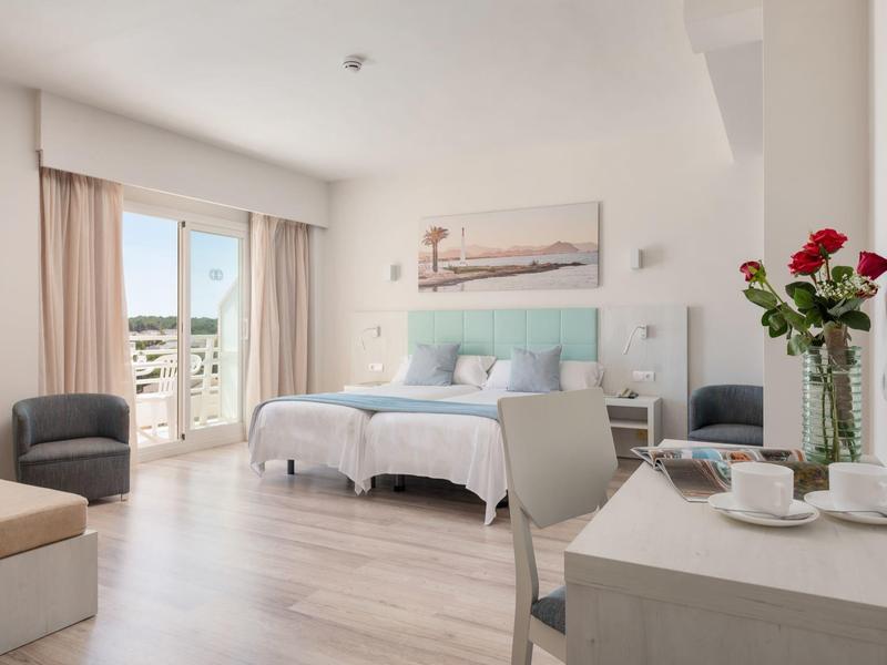 Habitación de hotel moderna con cama doble, mesa, sillas y balcón con vista a la ciudad.