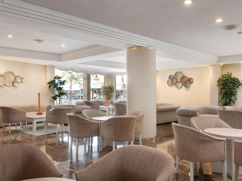 Área de descanso moderna y luminosa del hotel con sillones suaves, mesas y elementos decorativos en la pared.