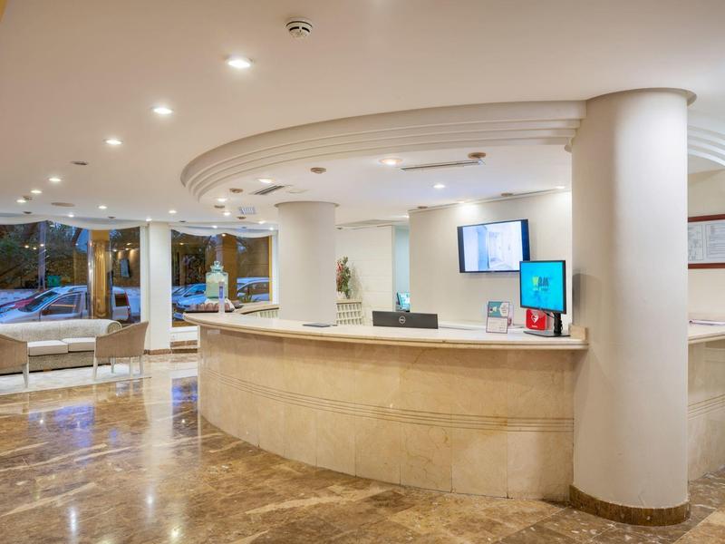 Área de recepción de hotel luminosa con mostrador curvo y zona de asientos junto a la ventana.