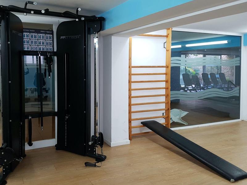 Sala de entrenamiento moderna con equipo de fitness multifuncional y banco de pesas junto a pared con espejo.