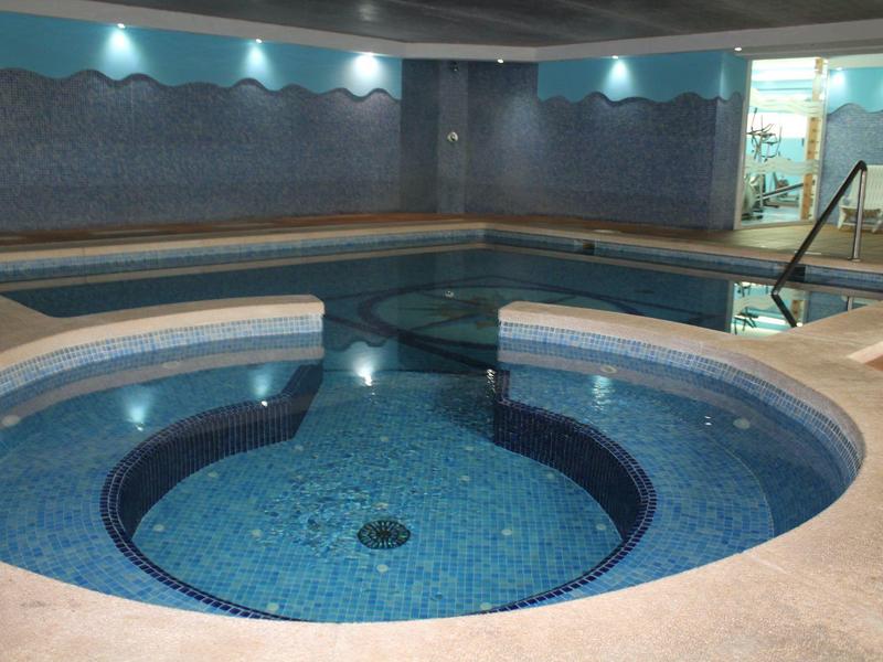 Un jacuzzi redondo con azulejos azules junto a una piscina rectangular en un espacio interior.