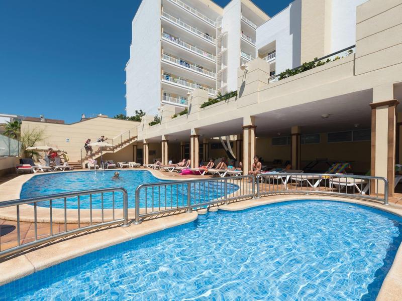 Dos piscinas al aire libre junto a un edificio de hotel de varios pisos bajo un cielo azul despejado.