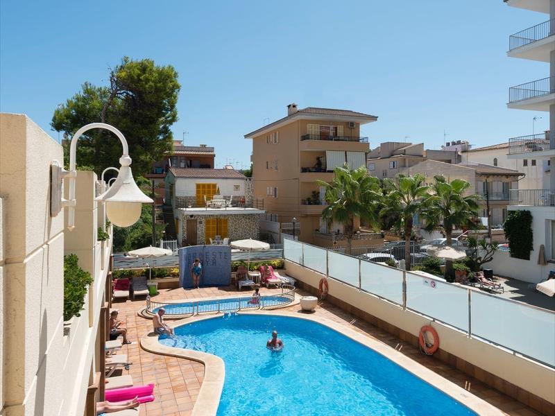 Piscina con sombrillas y tumbonas al lado de un hotel bajo cielo despejado.