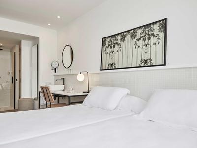 Moderní hotelový pokoj se dvěma postelemi, psacím stolem, židlí a abstraktní výzdobou na stěně.