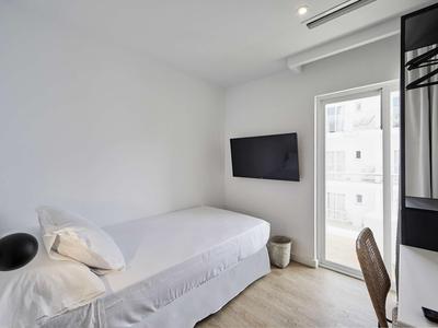 Malý, jednoduše zařízený hotelový pokoj s jednolůžkem a televizí na zdi.