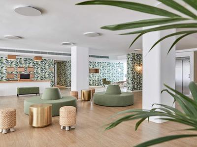 Moderní hotelová lobby s zeleným posezením a dekorativním vzorem na stěně.