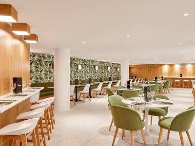 Moderní hotelový salonek se zelenými židlemi, dřevěnými doplňky a stylovým osvětlením.