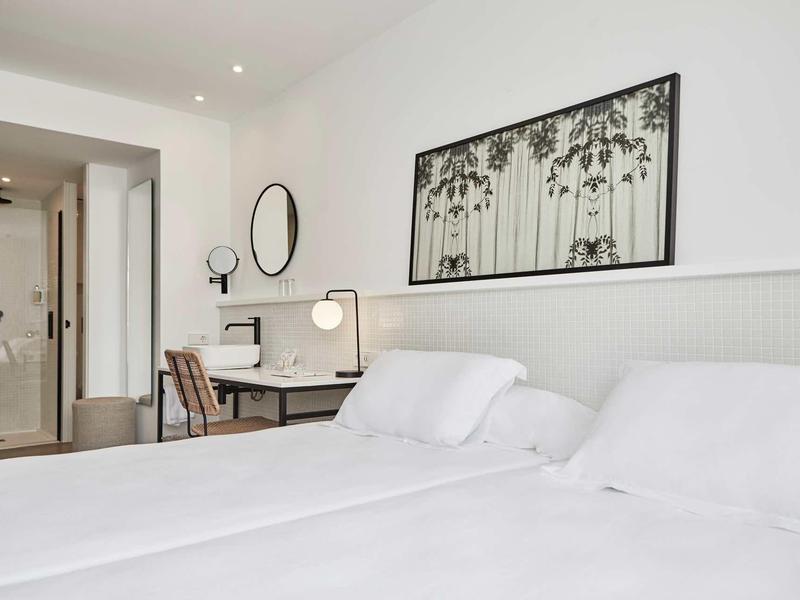 Moderní hotelový pokoj se dvěma postelemi, psacím stolem, židlí a abstraktní výzdobou na stěně.