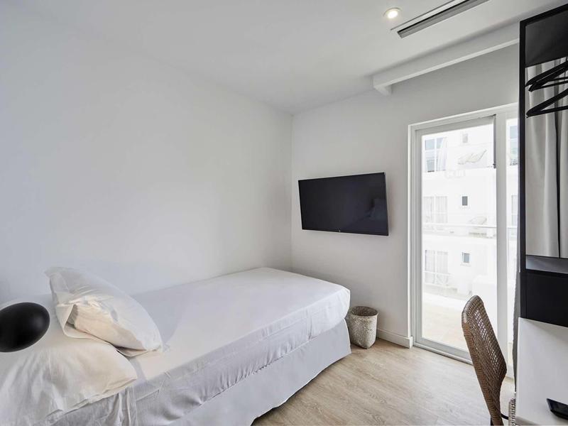 Malý, jednoduše zařízený hotelový pokoj s jednolůžkem a televizí na zdi.