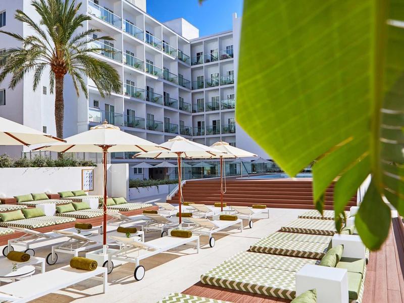 Hotelová bazénová oblast s lehátky a slunečníky vedle vícepodlažní budovy a palem
