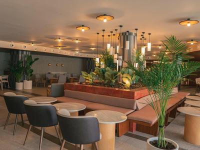 Elegancka część wypoczynkowa hotelu z miejscami do siedzenia i licznymi roślinami w nowoczesnym stylu.