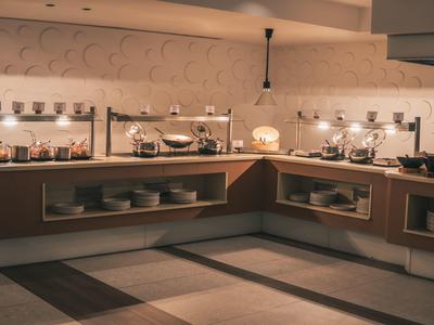 Nowoczesna strefa bufetu z oświetlonym jedzeniem i naczyniami w kuchni hotelowej.