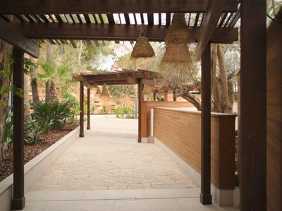 Allée couverte avec poutres en bois et lampes traversant un jardin soigné.