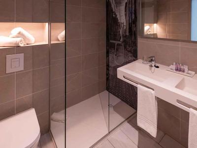 Nowoczesna łazienka z prysznicem bez brodzika, białą toaletą i umywalką z uchwytem na ręcznik.