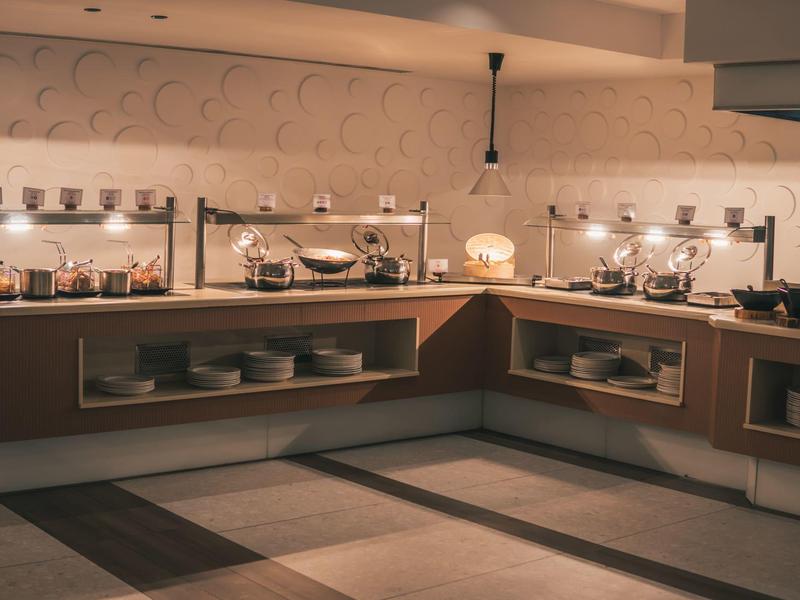 Nowoczesna strefa bufetu z oświetlonym jedzeniem i naczyniami w kuchni hotelowej.