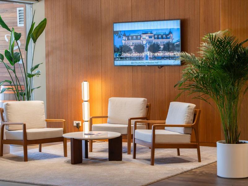 Salon z czterema fotelami, okrągłym stołem, roślinami i obrazem na ścianie w drewnianym wnętrzu.