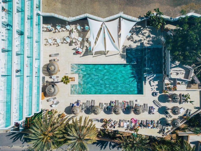 Widok z lotu ptaka na hotel z centralnym basenem i leżakami po bokach.