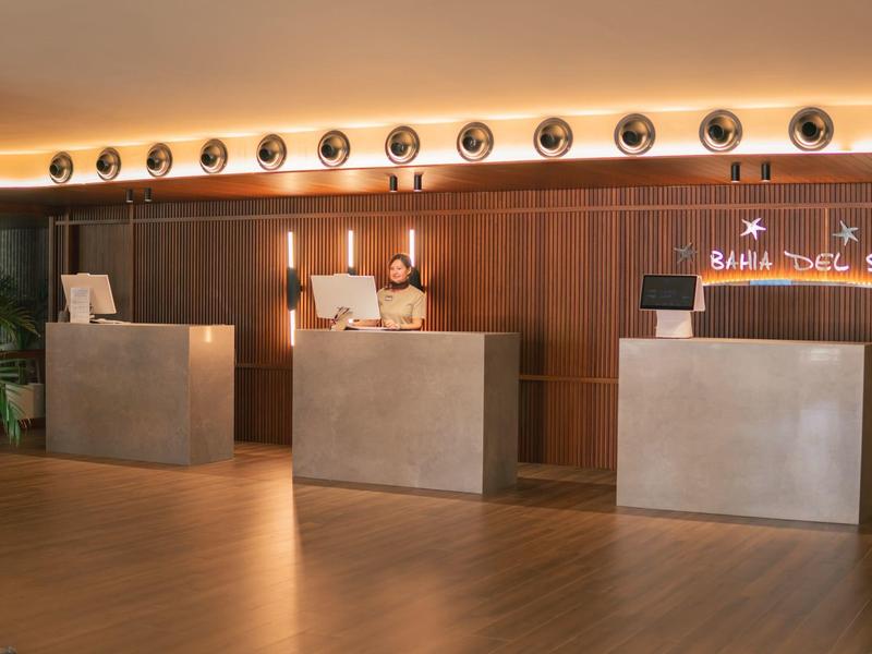 Nowoczesna recepcja hotelowa z trzema kamiennymi ladami i ciepłym drewnianym wykończeniem ściany