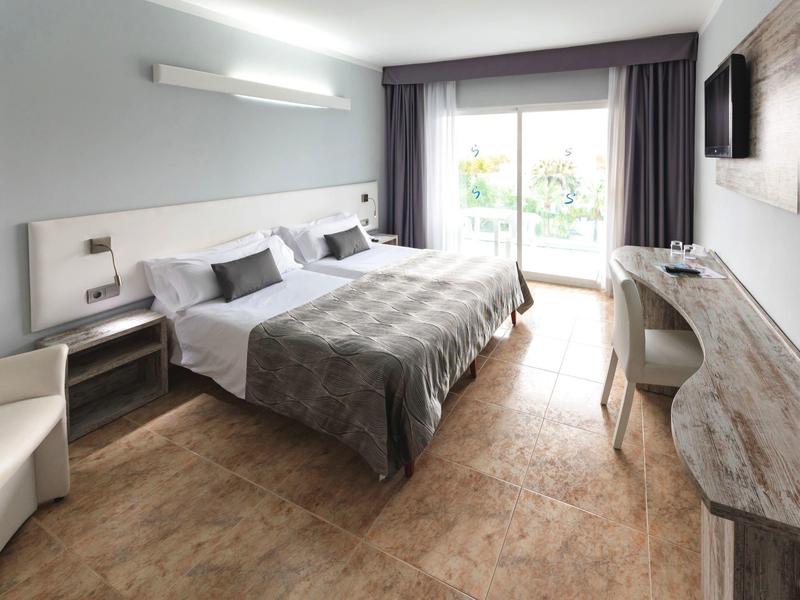 Nowoczesny pokój hotelowy z łóżkiem podwójnym, biurkiem i balkonem z dużą ilością naturalnego światła.