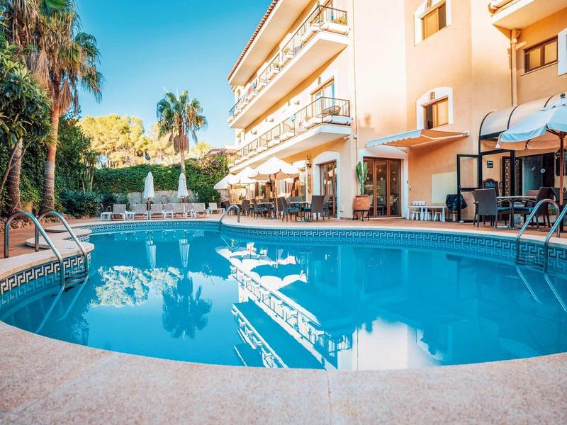 Piscina rotonda con lettini e ombrelloni accanto a un edificio alberghiero a più piani.