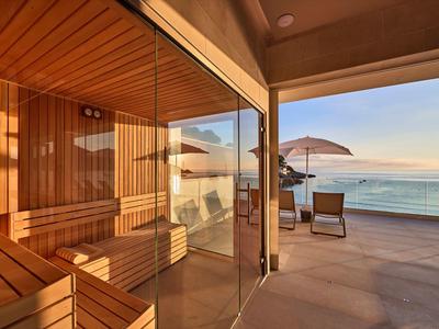 Moderne hotel sauna met glazen wand naar balkon en zeezicht bij zonsondergang.