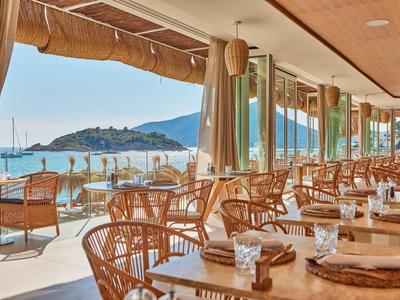 Open strandterras met houten tafels, stoelen en uitzicht op de zee en een eiland.