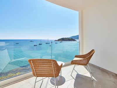 Balkon met twee stoelen en een tafel met uitzicht op zee en boten.