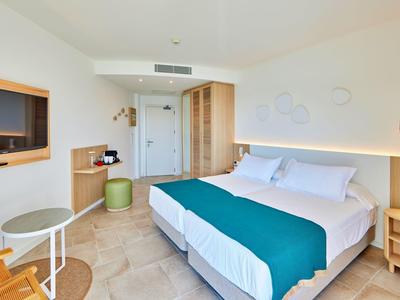 Lichte hotelkamer met tweepersoonsbed, turquoise bedloper en moderne inrichting.