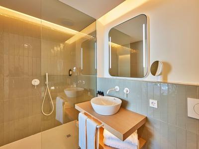 Moderne badkamer met glazen douche, wasbak op houten plank en verlichte spiegel.